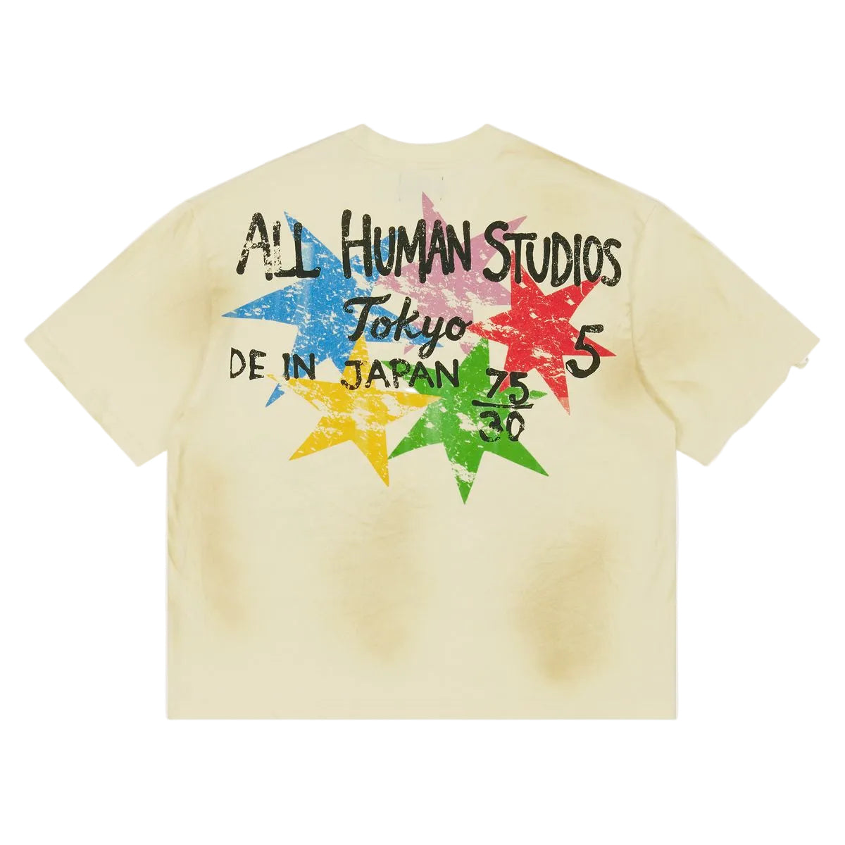 A pale yellow t-shirt shown from the back, featuring a large graphic print with the text 'ALL HUMAN STUDIOS Tokyo 5 DE IN JAPAN 75 80' over a distressed multicolor star design in blue, pink, red, yellow, and green.