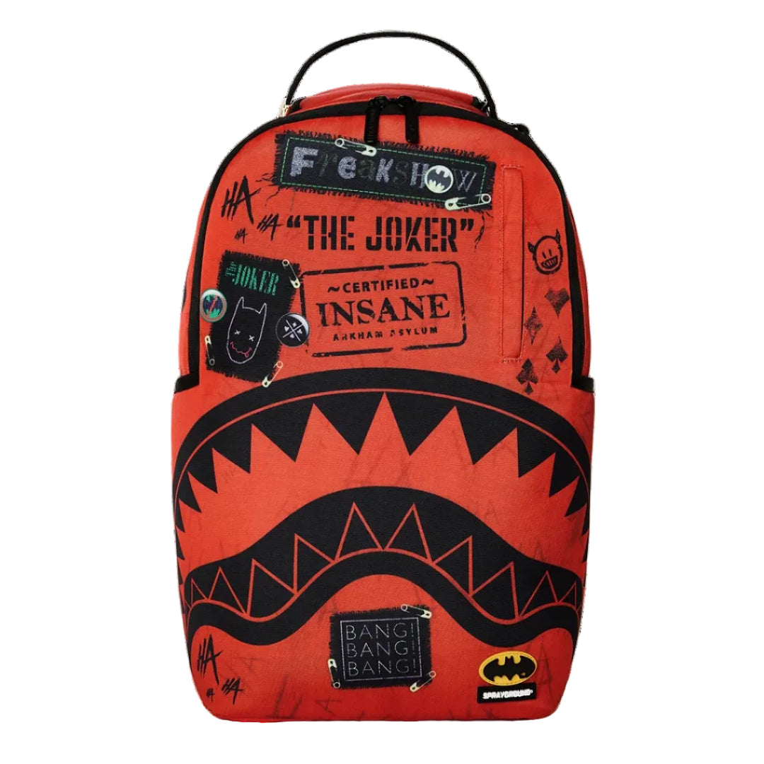 A bright orange-red backpack featuring a black shark mouth graphic across the lower half, with distressed patches and text including 'F*CK YOU', 'THE JOKER', 'INSANE', and Batman logos, shown on a white background.